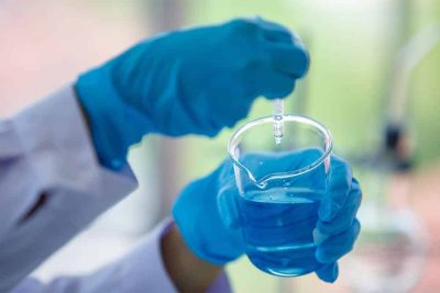 Close up hand laboratory beaker with blue liqid in analyst's hand in plastic glove blur background. Concept Science experiment